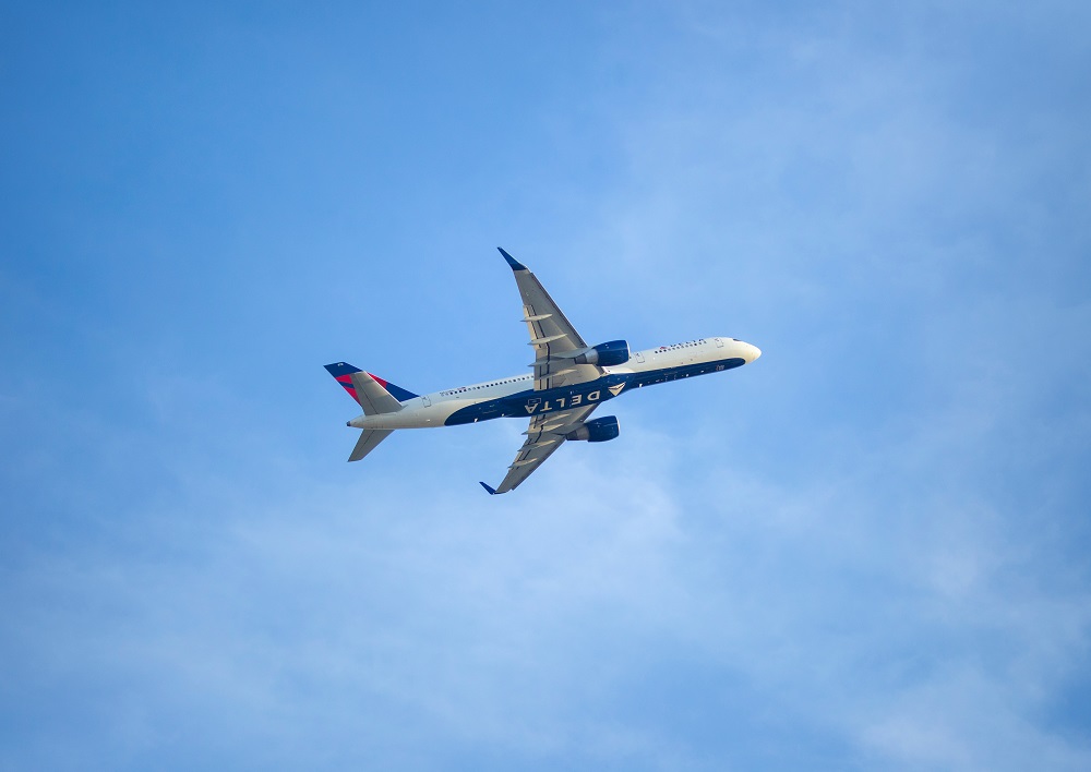 A Delta brand plane flies through clear blue skies. The picture is taken from the ground.